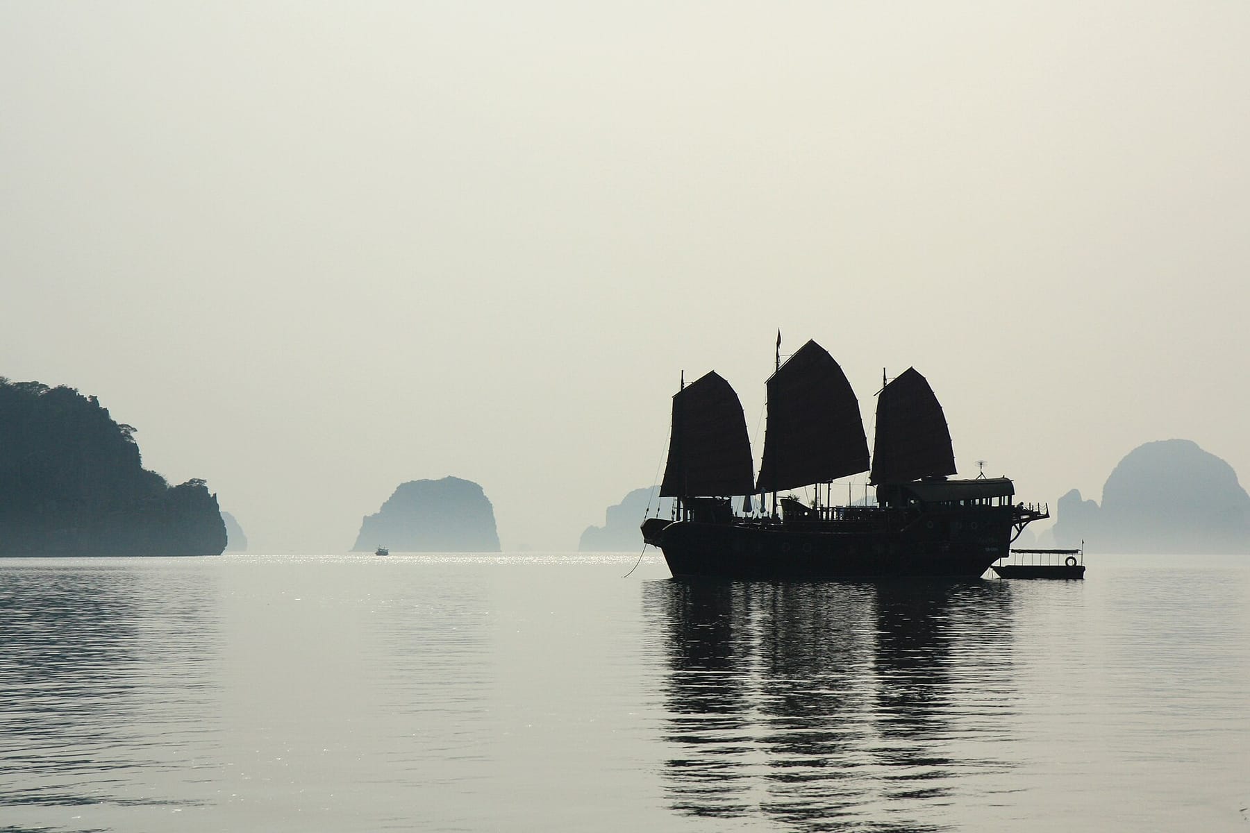 A single junk under sail on still, misty water in Ha Long Bay